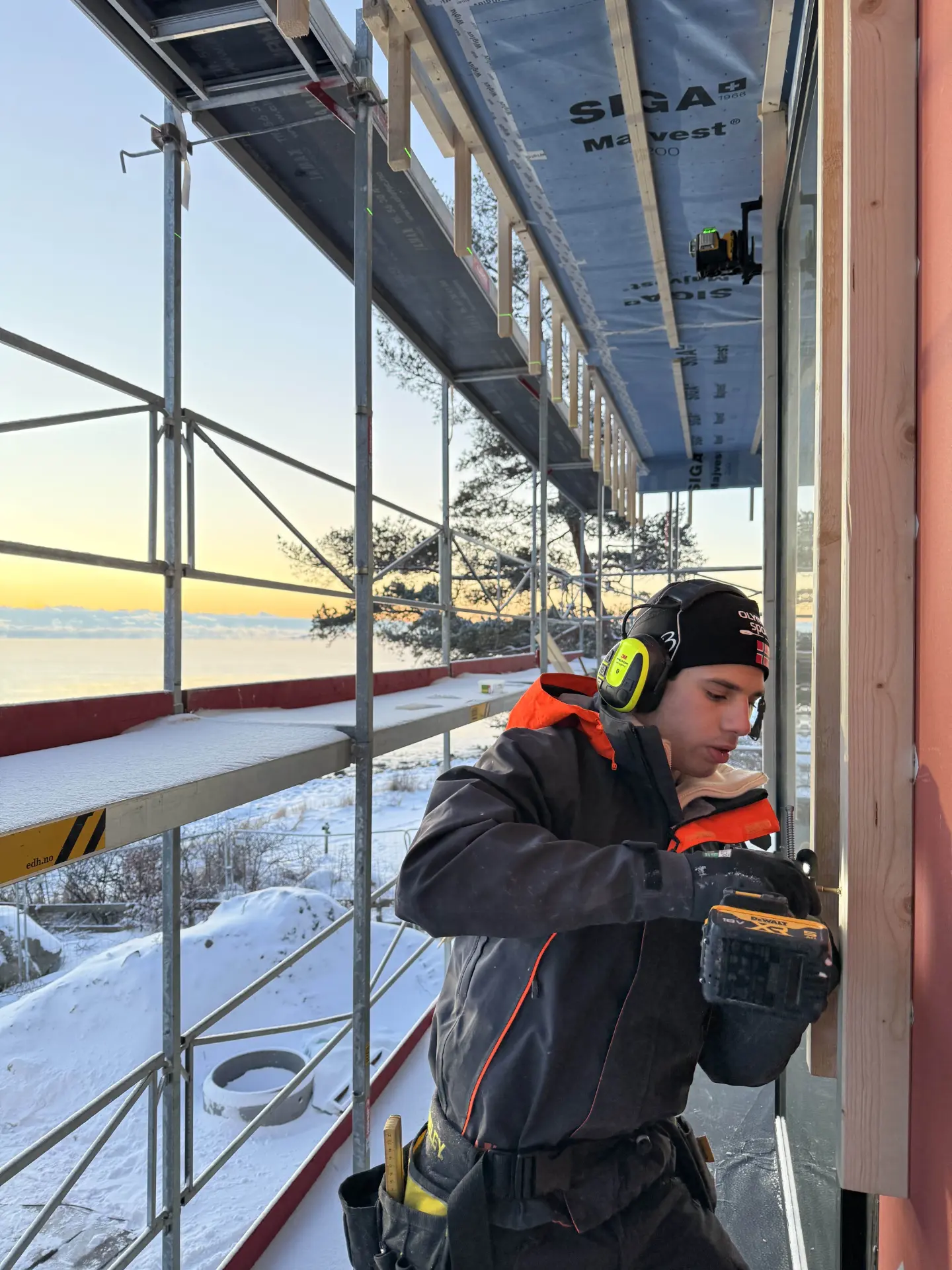 Tømrer monterer vindu i fasade med vindsperre og stillas rundt bygget