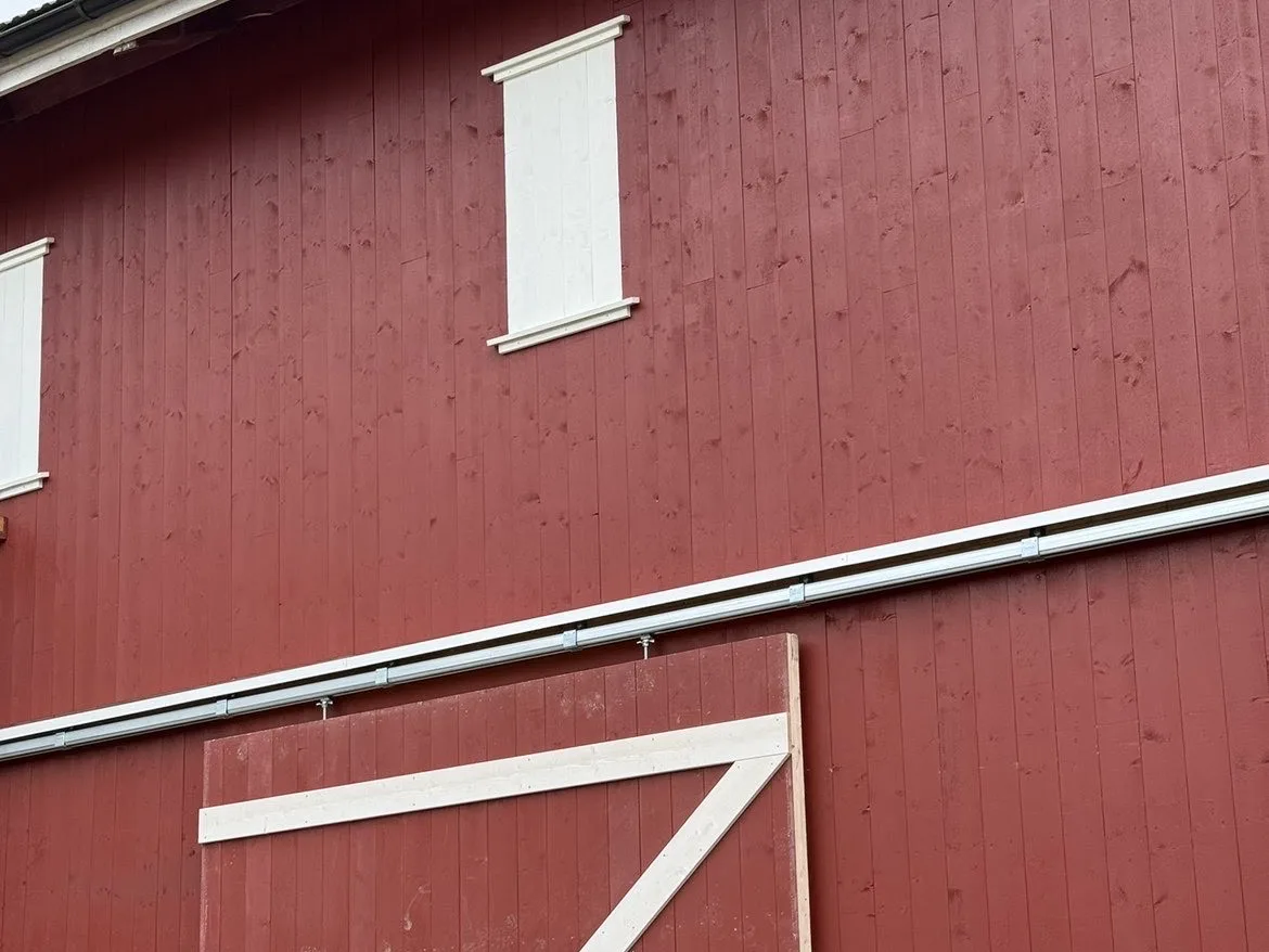 Rødmalt trebygning med stavende panel, hvite vinduslemmer og stor skyvedør