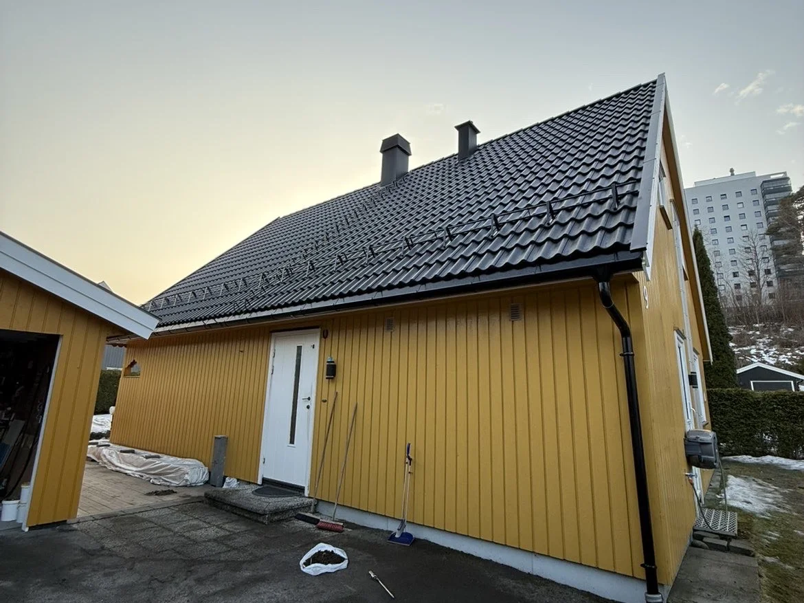 Gul bolig med nytt tak i svarte takstein, snøfangere og nye renner
